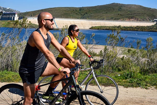 Un hombre y una mujer andan en bicicleta por un camino de tierra cerca de un cuerpo de agua en Privada Cobalto.
